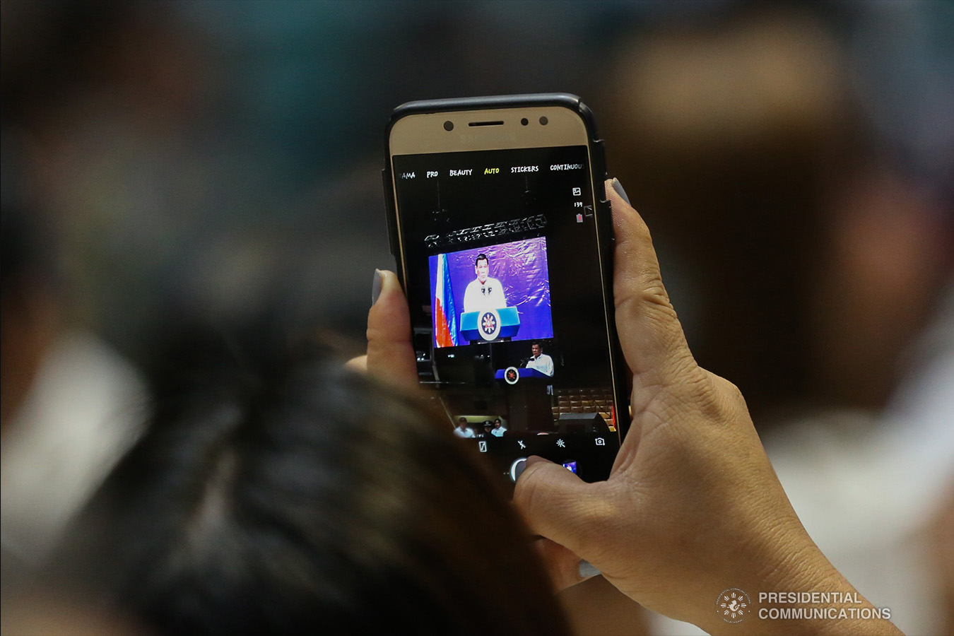A guest takes a snapshot of President Rodrigo Roa Duterte as he delivers his speech during the Barangay Summit on Peace and Order at the Cuneta Astrodome in Pasay City on January 8, 2019. TOTO LOZANO/PRESIDENTIAL PHOTO